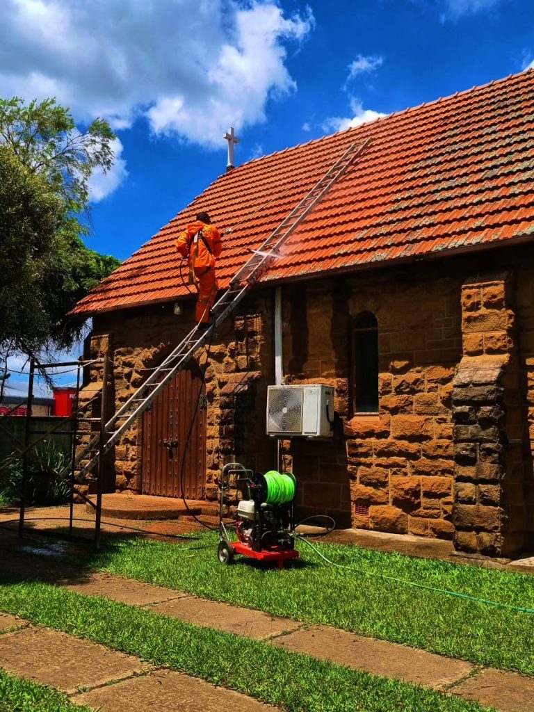 A professional painter using a jetting machine to spray the roof of a house.